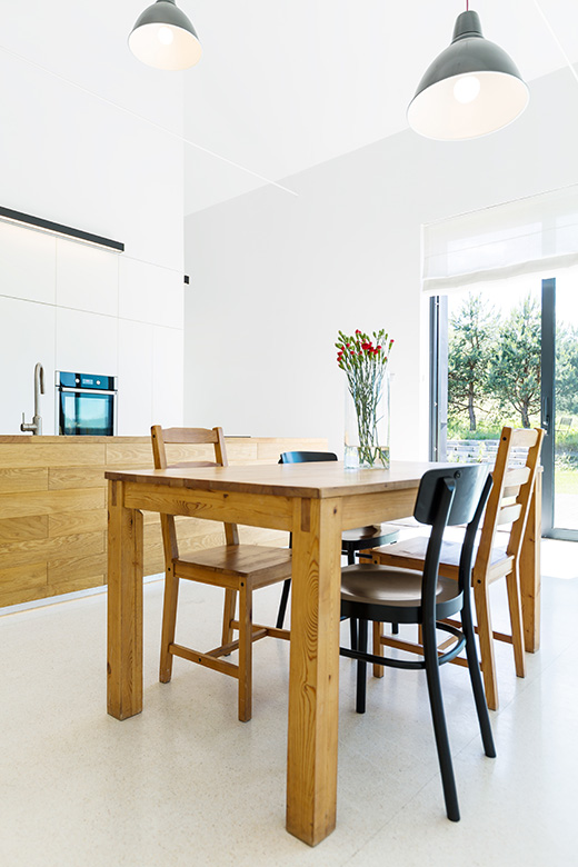 Image of a white house interior with big windows, simple wooden dining set, open kitchen